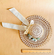Vintage crochet hat with faux flowers and golden ribbon, offering timeless elegance.
